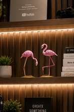 Load image into Gallery viewer, A cozy home office setup with a wooden desk, computer monitor, keyboard, and microphone, set against a slatted wood wall with warm LED lighting. Decorative pink flamingos, books, plants, and a framed YouTube award are displayed on the shelves.