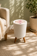 Load image into Gallery viewer, A ribbed white cylindrical side table with three wooden legs stands in a sunlit living room next to a beige armchair and a potted plant. The tabletop has a colorful floral pattern.