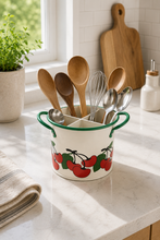 Load image into Gallery viewer, A white enamel kitchen utensil holder with green handles and a red cherry pattern, filled with wooden and metal kitchen utensils, set on a marble countertop in a bright kitchen.
