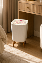 Load image into Gallery viewer, A white ribbed cylindrical stool with a floral-patterned lid sits in a sunlit bedroom next to a wooden vanity table.