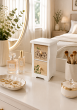 Load image into Gallery viewer, A small white wooden two-drawer vanity organizer with decorative bicycle and leaf motifs on the drawer fronts, styled on a white dresser beside perfume bottles, makeup brushes, jewelry, and a mirror in a bright bedroom setting.