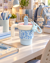 Load image into Gallery viewer, Blush Pink leopard-print water bottle with cream handle and pink carrying strap on a study desk.