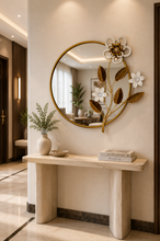Load image into Gallery viewer, Image Alt Text
Luxury round wall mirror with gold metal frame, white floral accents, and decorative botanical leaves displayed above a modern console table.