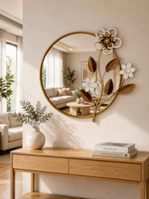 Load image into Gallery viewer, Image Alt Text
Luxury round wall mirror with gold metal frame, white floral accents, and decorative botanical leaves displayed above a modern console table.