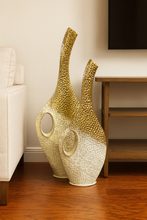 Load image into Gallery viewer, Modern sculptural gold-and-cream metal vases with open circular design placed on a wooden console.