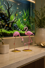 Load image into Gallery viewer, A modern interior scene featuring a large illuminated aquarium with green plants and small fish, set behind a marble console table. On the table are two pink flamingo figurines, a large beige ceramic vase with greenery, and a gold decorative bowl.
