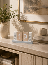 Load image into Gallery viewer, A wooden block calendar displaying August 19th, Wednesday, styled on a beige stone console table in a warm, sunlit room with a ceramic vase, framed art, and books.
