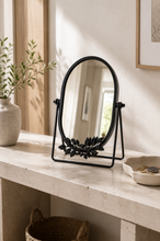 Load image into Gallery viewer, Black oval botanical tabletop vanity mirror with decorative metal leaf design on bedroom dresser – MetaphorBD
