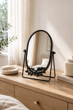 Load image into Gallery viewer, Black oval botanical tabletop vanity mirror with decorative metal leaf design on console table – MetaphorBD
