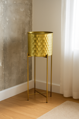 Tall golden honeycomb metal planter with stand placed in modern corner