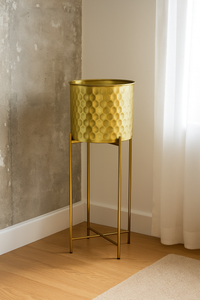 Tall golden honeycomb metal planter with stand placed in modern corner