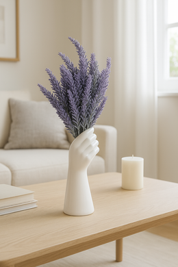 Hand-shaped white ceramic vase holding artificial lavender stems on a wooden shelf in front of a mirror