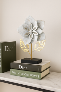 "Metal flower sculpture with white layered petals and golden leaves on black base"