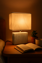 Load image into Gallery viewer, Ceramic table lamp with fabric shade on bedside table from MetaphorBD.
