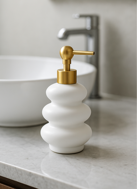 White ripple-shaped ceramic soap dispenser with gold pump on marble counter