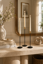 Load image into Gallery viewer, Three black and gold metal candle holders with battery-powered LED taper candles on a dining table
