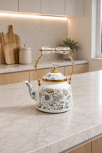 Load image into Gallery viewer, Floral enamel tea kettle in white with blue-grey floral pattern, gold-tone detailing and crystal-style accents, available in 1-liter and 2.4-liter capacities.
