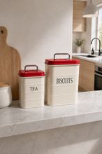 Load image into Gallery viewer, Retro Pantry metal Tea and Biscuit canister set with cream bodies and red lids on marble kitchen counter – MetaphorBD
